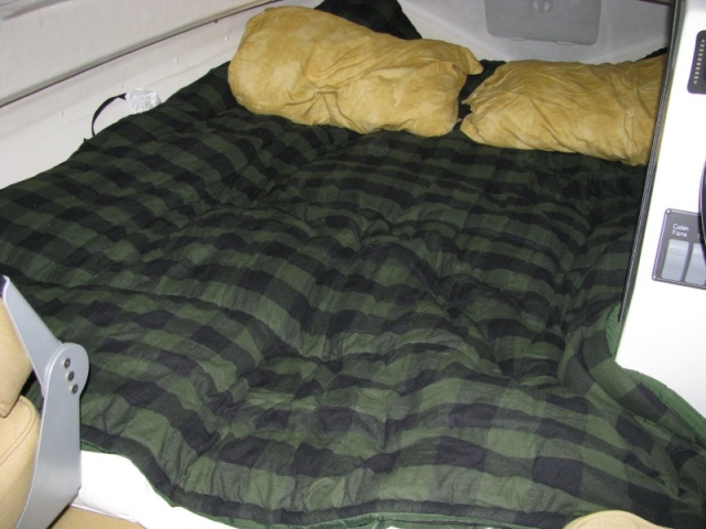 Fully extended berth showing head-first sleeping arrangement. Shown are two, queen size pillows.   We bought two flannel sleeping bags, good to 40 degrees, for $136 at LL Bean.  We unzipped them, using one for the bottom, which sat on top of our fiberbed topper, and the other was used as a comforter.  Overall, this sleep space is roughly 6 feet long by 5 feet wide, with a slight decrease to 4.5 feet at the bulkhead.  We slept better is this berth then we did at home.  9/26/12 comment.  This berth is a lot larger than one would think.  I can sleep across the bunker once past the bulkhead.  The only issue with sleeping toward the bow is the deck is close to one's head, but that's OK after awhile, since you have a cavernous view of the cabin from that perspective as well as having the hatch overhead.  Another thing that should be considered is that if any of you suffer from heartburn like I do, you know that it is infinitely preferable for your head to be higher then your feet.  Sleeping with your head toward the bow achieves this.