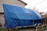 Port view of tarp tied to the frame of the trailer with bungee cords and lines.