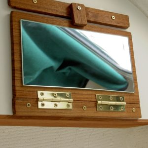 Media 'Vanity mirror: in folded mode, secured to bottom of shelf.' in album 'Valkyrie: Fold-down vanity mirror is glued to teak. Brass hinges and screws are used.  In response to a few PM's: the mirror wasn't centered on the aisle because that space is reserved for future projects.  The mirror is only sightly above the other seat, but can easily be used when standing in the aisle.'