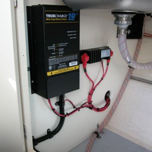 True Charge 10 Amp battery charger mounted under galley on front bulkhead on the left, Blue Sea Systems CL-Series BatteryLink a battery combiner on the right