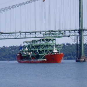 First section being lifted by orange winches on base of tower. Ship will move to the left, and winches will lower road piece onto lifting barge.