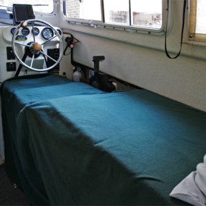 Media 'Starboard side made up into 6 ft + bed by lowering galley covers, adding extender cushion and support, then removing seatback and moving to front of bottom. Seat back is held by strap around steering wheel snapped into the existing snaps on the seatback. A support slides out from under seat bottom to support the seatback; very simple to deploy.' in album 'Port and Starboard Beds looking aft. The kitchen storage pocket is removed from the helm seat back and snapped to the cabin door when the starboard bed is setup.'