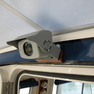 CCD camera  above the cabin door. Horizontal field of view = 90 deg., vert. field of view = 20 deg.. It has a built in mic within the camera head body. Volume can be muted or controlled at the monitor under the 'MODE' function - very handy when running with the door closed. The wedge is a cedar shingle cut to provide the necessary vert. angular range for the bracket supplied. A single multiconductor small cable  is fed straight into the cabin and routed along the port side wiring harness directly to the monitor, where the camera also gets its power.