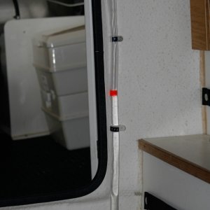 Media 'Water Tank Sight Tube added to allow quick monitoring of water level in tank inside port storage enclosure. Black label tape on the tube clamps mark 1/2 and Full Levels. One end of the tube tees into the 1/2 inch tube exiting the bottom of the tank and the other end tees back into the vent tube exiting the top of the tank. I got the idea of a colored ball or float from Sea Wolf (thanks, Joe).' in album 'Copilot storage made from lucite sheet cut, heated and formed into a simple L shape. Mounted to forward bulkhead and seat box. Teak trim stiffens and covers the top edge.'