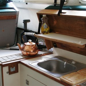 Media 'Galley-sink-and-cover' in album 'Covers are raised and helm seat pivots up to use galley. Hot items can be placed on ceramic tiles under helm seat. Small drop-down shelf inside forward cover is made of starboard trimmed in teak. Snap on elastic bands are handy for holding essentials (spelled COFFEE press) when underway.'