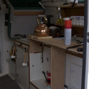 Media 'Starboard bed support provides useful counter space for galley. Drop down foot support shown in background' in album 'Covers are raised and helm seat pivots up to use galley. Hot items can be placed on ceramic tiles under helm seat. Small drop-down shelf inside forward cover is made of starboard trimmed in teak. Snap on elastic bands are handy for holding essentials (spelled COFFEE press) when underway.'