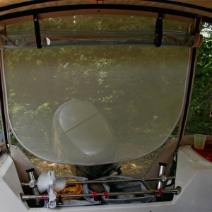 Looking aft with camperback window rolled up to expose screening. We are told that the screening blocks visibility from the rear, although we see fine from inside. Fan clamps to transom bars and makes a big difference in hot weather. Nylon mesh bags sit down inside bars to hold drinks, water jugs, and propane cylinders kept in a porous nylon bag. Any leakage should go out of the splash well outlet. We normally lash a large cooler on the bars when underway to free up floor space. Rear panel goes behind lazerettes to free up significant space.