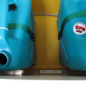 The yellow Starboard? platform with white cleats was set up for my original water tank, which then sprung a leak.  I'm planning to get a new/permanent tank, but in the meantime set up this system.  A temporary full width Starboard cleat holds the jugs off the upper/inboard locker side.  Three jugs just fit, with storage outboard (behind them).
