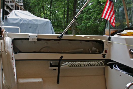 Added washdown pump under starboard lazerette and waterproof 12 V outlet. Bracket to hold magma cooking surface mounted with starboard spacer. The washdown is configured to take water from either the fresh water tank or externally. Added the red switch cover to reduce chance of accidentally energizing pump and to give visual indication that the pump is powered on. The water source can be easily switched between internal and external with a simple valve. Nylon strap / snaps in front of washdown hose secures starboard Coleman chair for trailering. Life buoy at far left is mounted to starboard aft wall of pilot house for quick deployment.