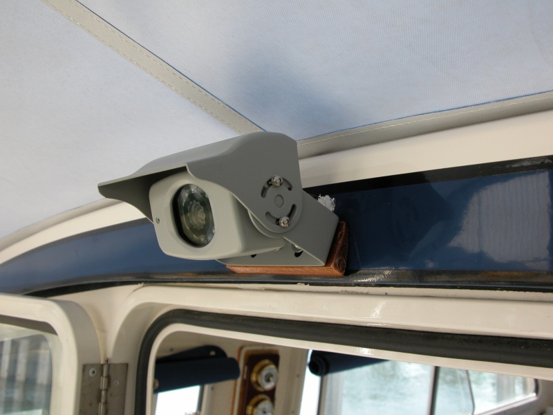 CCD camera  above the cabin door. Horizontal field of view = 90 deg., vert. field of view = 20 deg.. It has a built in mic within the camera head body. Volume can be muted or controlled at the monitor under the 'MODE' function - very handy when running with the door closed. The wedge is a cedar shingle cut to provide the necessary vert. angular range for the bracket supplied. A single multiconductor small cable  is fed straight into the cabin and routed along the port side wiring harness directly to the monitor, where the camera also gets its power.