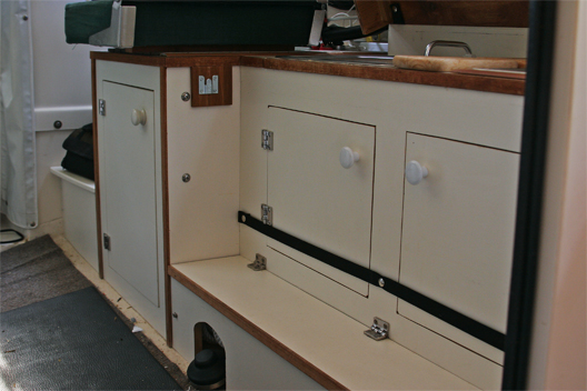 Galley cabinets were cut into the starboard seat box. Hinged lid covers long box used to hold rope, tools and other stuff. The whale foot pump works great and conserves water. At left of top center is a clip that mates with fingers on the starboard bed support.