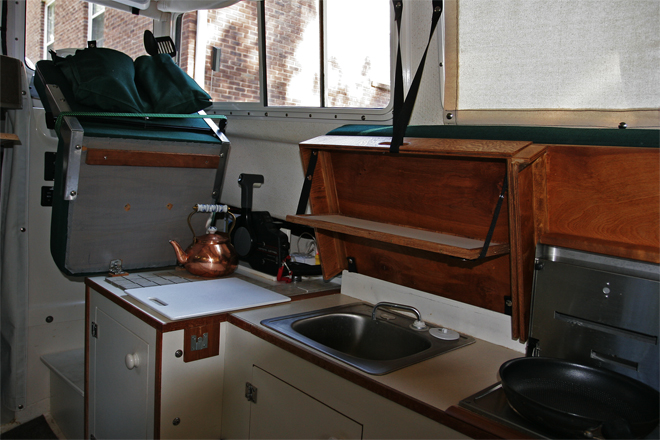 Galley from cabin door. Sunbrella pocket snapped to back of helm seat holds kitchen untensils, cups, plates and other stuff. Helm seat can be hinged up to give access to substantilly more counter space covered with ceramic tile for hot items.