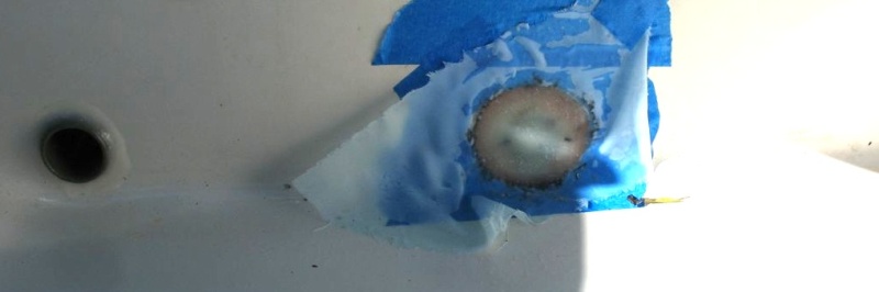 Here I have fiberglassed over the depression.  I started with neat resin, then leveled the center with thickened epoxy (colloidial silica), and then added concentric layers of 10 oz. cloth.  I added some peel ply (release cloth) over the top to smooth it - that's the "windbreakery" looking stuff you can see.  You can see the "real" drain over to the left in the photo.