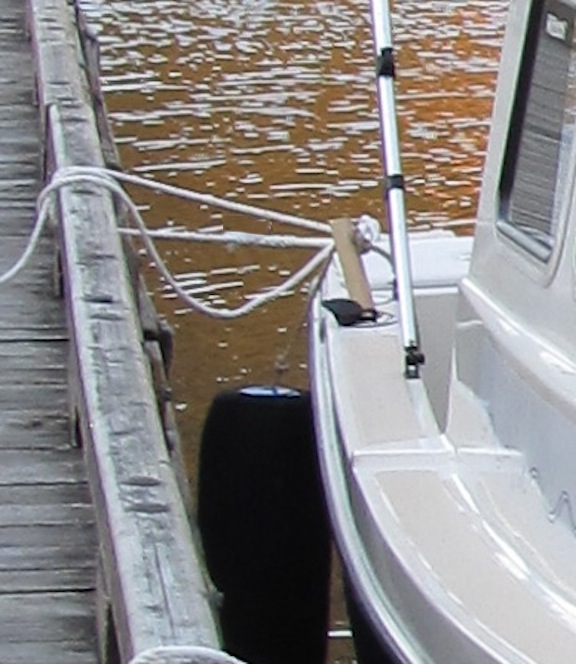 Not the best photo - I'll try to get a better one in future.  This is an alternative method of hanging the after fender.  I got the idea from Will-C and wanted to try it since the fender hanging from the after cleat can tend to get aft of the boat.  The basic idea is to put some sort of dowel into the rod holder (these were already in my boat) and then hang the fender from it.  I started with Schedule 80 PVC pipe (1" IIRC), but didn't really like handling it, so this is an ash tool handle replacement (bought at Ace Hardware).  To secure the fender whip to the dowel, I drilled a hole through the dowel, and then run the whip through it and then tie a figure-8 knot.  That way it is adjustable if necessary.  I left the dowel this long because it then keeps the whip/line off the gelcoat at the edge of the deck.