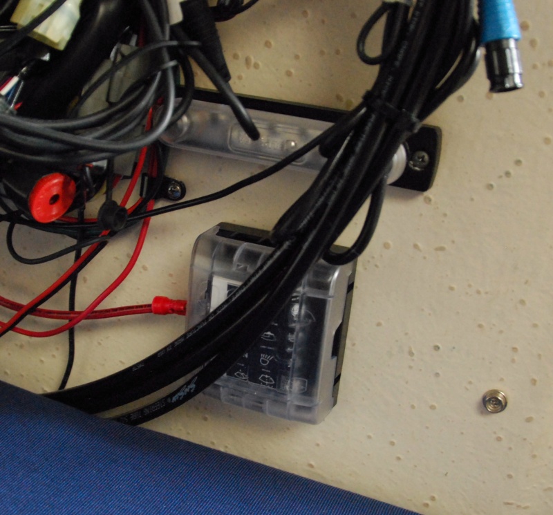 Sea Angel\'s Secondary AUX 6 ckt DC power block & 10x ground buss 2a. The rectanguliar 'bar' above the square Secondary AUX DC power panel is a 10X #8-32 negative ground buss bar. It has a plastic removeable protective push on cover. It is strapped to the main 12 ckt MAIN AUX Negative ground stud post with a copper link. 
The black "cables" laying above the power blocks are the steering's hydraulic lines.
