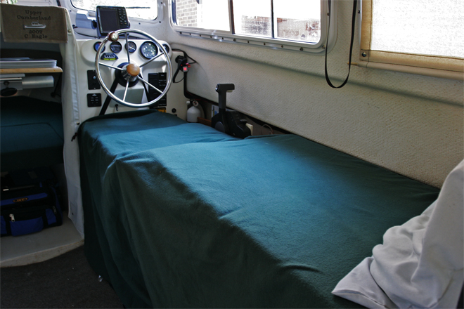 Starboard side made up into 6 ft + bed by lowering galley covers, adding extender cushion and support, then removing seatback and moving to front of bottom. Seat back is held by strap around steering wheel snapped into the existing snaps on the seatback. A support slides out from under seat bottom to support the seatback; very simple to deploy.