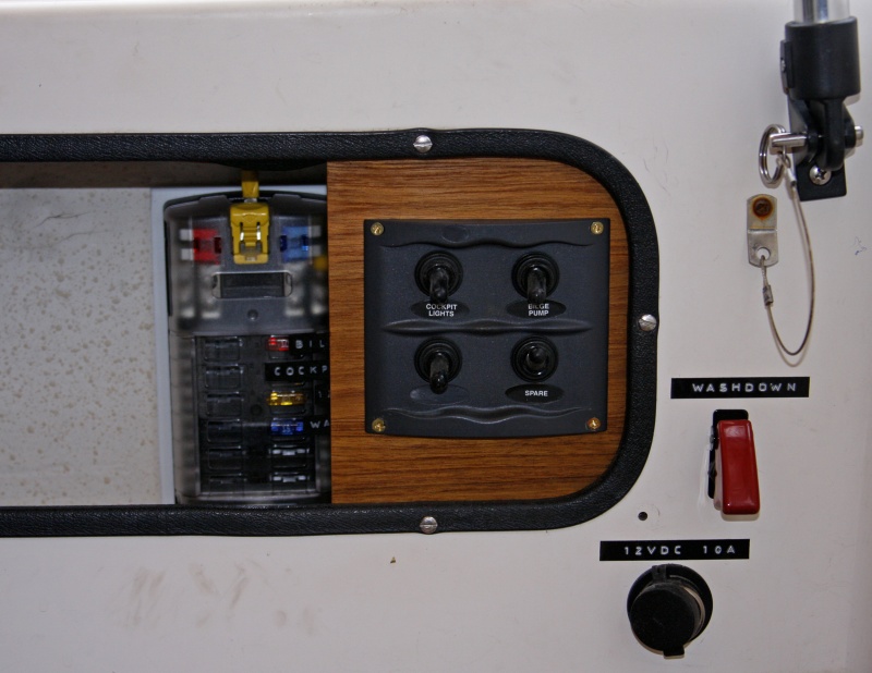Switch Panel mounted on teak includes switches for port and starboard LED lights, additional Rule 1100 bilge pump plus one spare. Covered fuse panel to left is accessible and labeled.