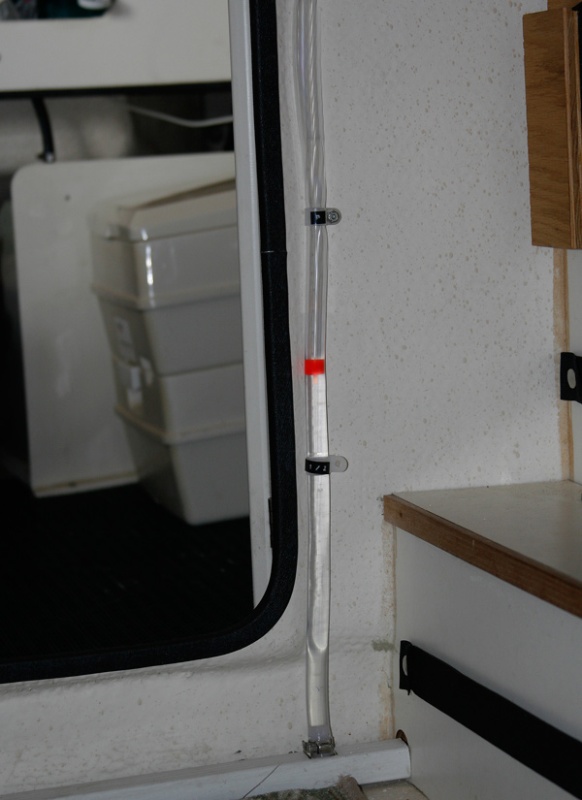 Water Tank Sight Tube added to allow quick monitoring of water level in tank inside port storage enclosure. Black label tape on the tube clamps mark 1/2 and Full Levels. One end of the tube tees into the 1/2 inch tube exiting the bottom of the tank and the other end tees back into the vent tube exiting the top of the tank. I got the idea of a colored ball or float from Sea Wolf (thanks, Joe).